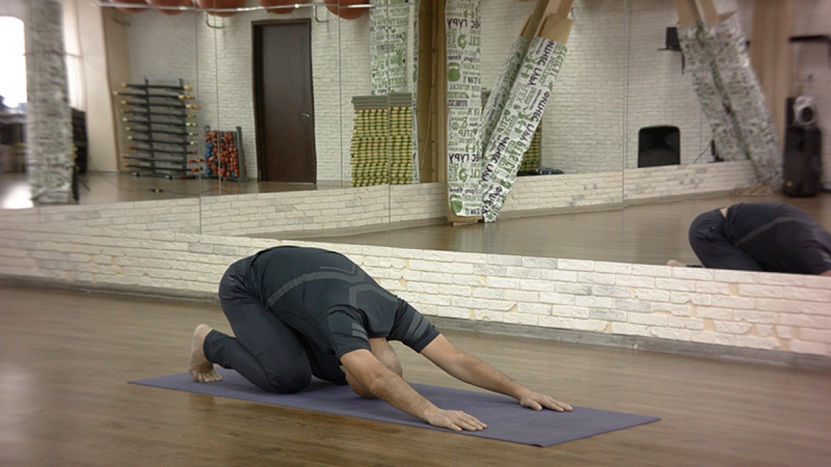 Man resting on a yoga mat in Balasana, Child's Pose, forehead down and arms forward