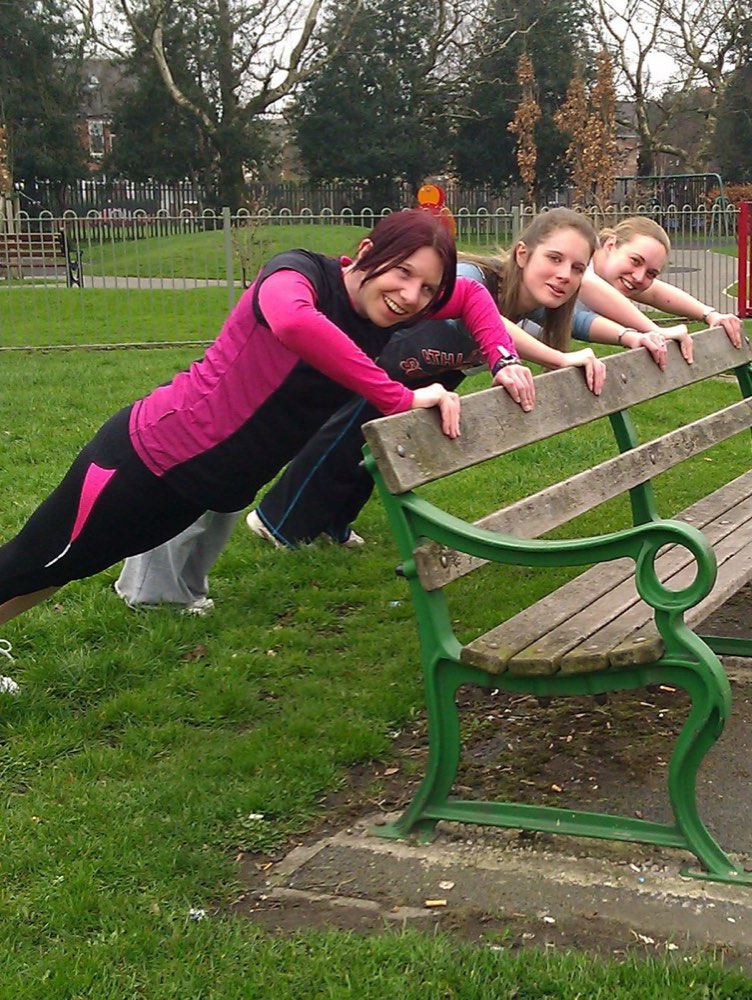 People doing incline push-ups against a park bench